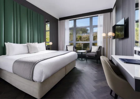 Spacious modern hotel room with king bed, large windows, sleek decor, and smart TV, offering tranquil garden views.