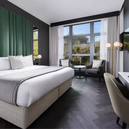 Spacious modern hotel room with king bed, large windows, sleek decor, and smart TV, offering tranquil garden views.