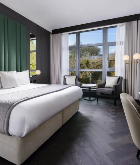 Spacious modern hotel room with king bed, large windows, sleek decor, and smart TV, offering tranquil garden views.