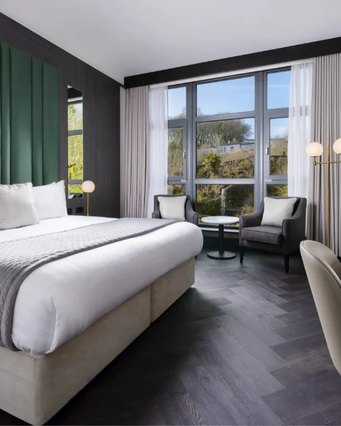Spacious modern hotel room with king bed, large windows, sleek decor, and smart TV, offering tranquil garden views.