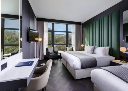 Spacious modern hotel room with king bed, large windows with scenic view, seating area, TV, and elegant decor.