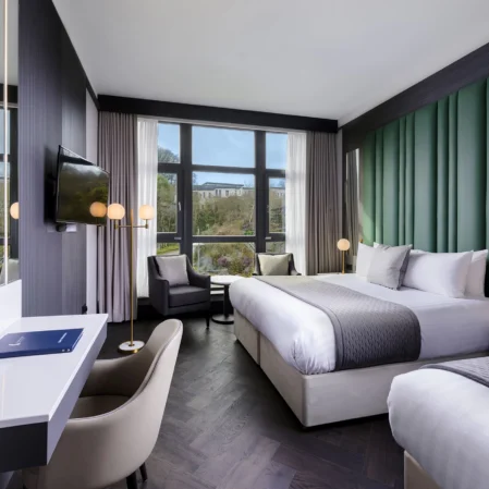 Spacious modern hotel room with king bed, large windows with scenic view, seating area, TV, and elegant decor.