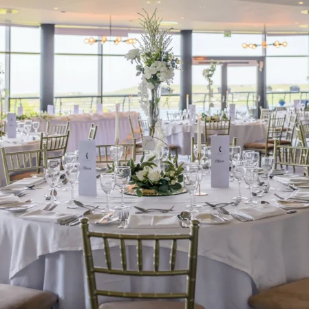 Elegant banquet hall set for a wedding, featuring round tables, white linens, flower centrepieces, and panoramic countryside views.