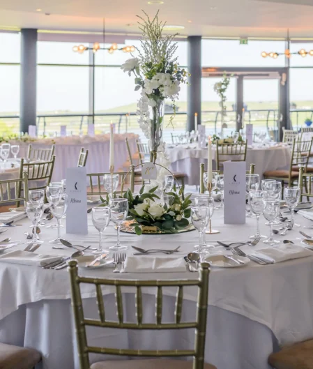 Elegant banquet hall set for a wedding, featuring round tables, white linens, flower centrepieces, and panoramic countryside views.