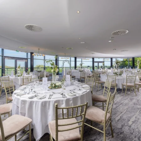 Elegant banquet hall with panoramic views, set for a wedding with white linens and golden chairs, perfect for events.