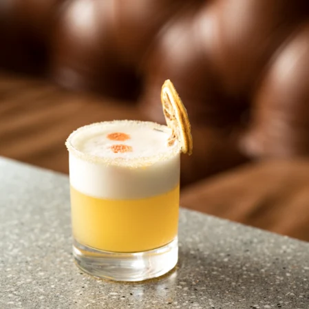 Elegant cocktail with citrus garnish on granite bar, luxurious leather sofa in background, perfect for a relaxing evening.