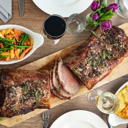 Luxurious roast beef dinner with vegetables and gratin potatoes, complemented by wine, in a stylish hotel dining setting.