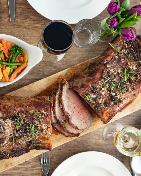 Luxurious roast beef dinner with vegetables and gratin potatoes, complemented by wine, in a stylish hotel dining setting.