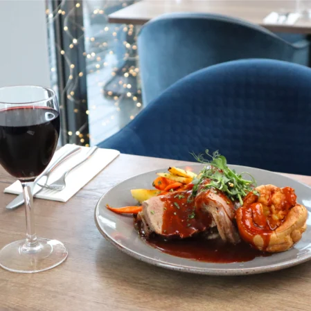Savour roast dinner with wine in elegant restaurant, featuring plush blue chairs and twinkling lights for a cosy dining experience.