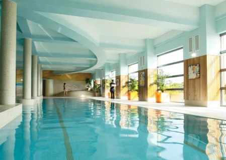 Luxurious indoor pool with large windows, skylight, and sunlit loungers for ultimate relaxation at our modern hotel.