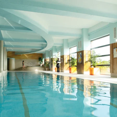 Luxurious indoor pool with large windows, skylight, and sunlit loungers for ultimate relaxation at our modern hotel.