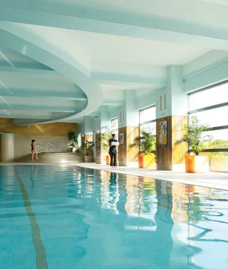 Luxurious indoor pool with large windows, skylight, and sunlit loungers for ultimate relaxation at our modern hotel.