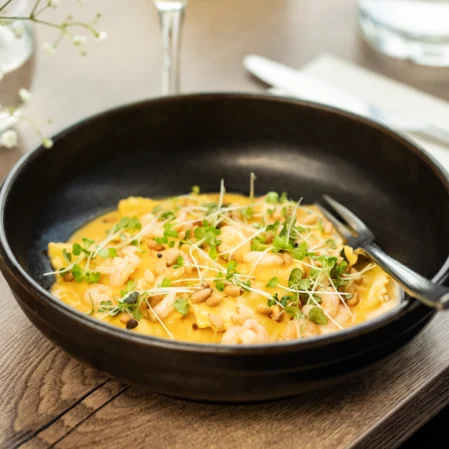 Exquisite shrimp and microgreen ravioli dish in a black bowl at a luxury hotel restaurant, featuring elegant table setting.