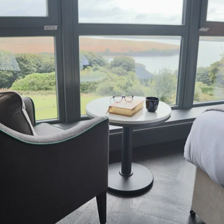 Bright hotel room with stunning lake view, comfy armchair, cosy bed, and amenities for a relaxing stay.