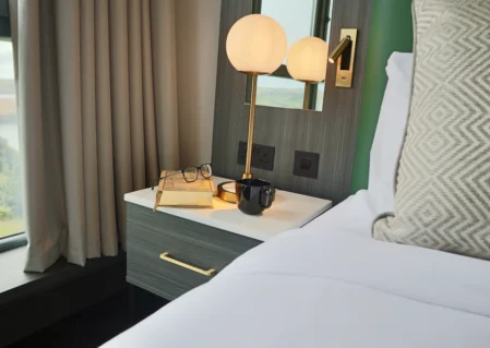 Cosy hotel room with comfortable bed, bedside table, lamp, scenic window view, perfect for a relaxing stay.