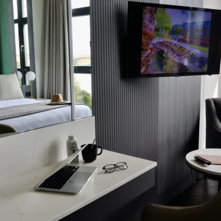 Modern hotel room with comfy bed, workspace, flat-screen TV, and city view, perfect for business or leisure stays.