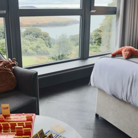 Spacious hotel room with river view, cosy seating, plush bed, and fun games, perfect for a relaxing stay.