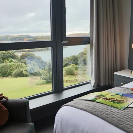 Scenic countryside view from cosy hotel room window, featuring plush bed and armchair for relaxation.