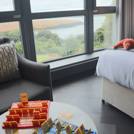 Stylish hotel room with panoramic sea view, comfy seating, plush bed, and board game, near scenic coastline retreat.