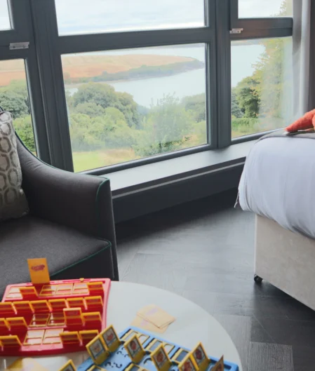 Stylish hotel room with panoramic sea view, comfy seating, plush bed, and board game, near scenic coastline retreat.