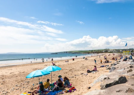 Guests enjoy sun and sea views on sandy beach with bright blue umbrellas; coastal relaxation and scenic coastline nearby.