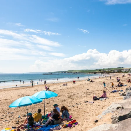 Guests enjoy sun and sea views on sandy beach with bright blue umbrellas; coastal relaxation and scenic coastline nearby.