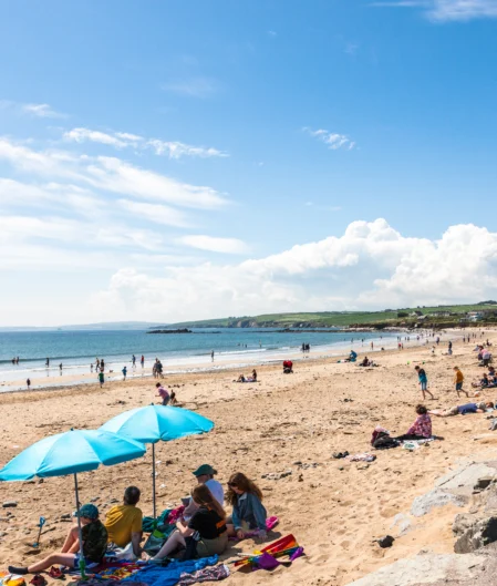 Guests enjoy sun and sea views on sandy beach with bright blue umbrellas; coastal relaxation and scenic coastline nearby.