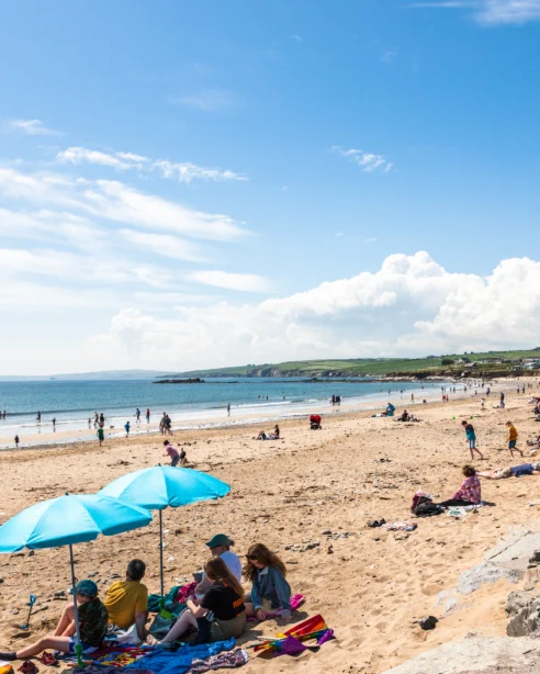 Guests enjoy sun and sea views on sandy beach with bright blue umbrellas; coastal relaxation and scenic coastline nearby.