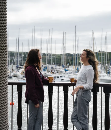 Two guests enjoying coffee on a balcony overlooking a scenic marina with sailboats at luxury hotel.