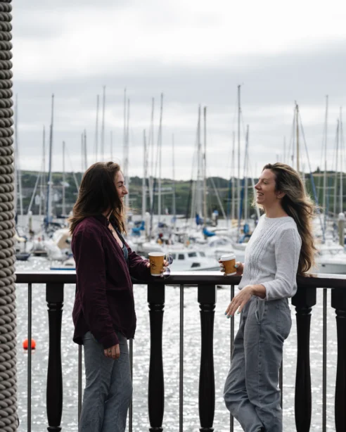Two guests enjoying coffee on a balcony overlooking a scenic marina with sailboats at luxury hotel.