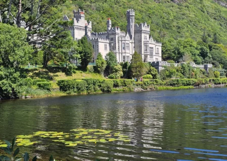 Scenic view of castle hotel by tranquil lake surrounded by lush greenery, offering a serene retreat and historic charm.