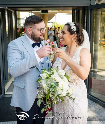 Bride and groom toast with champagne outside elegant hotel entrance adorned with flowers.