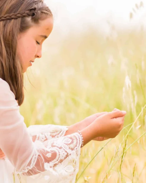 Young girl exploring serene meadow with soft sunlight, wearing a lace dress, embodying tranquil nature retreat experience.