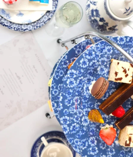 Elegant afternoon tea set with desserts on blue floral china, tea pot, and menu at luxury hotel restaurant.
