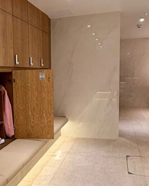 Elegant hotel changing room with wooden lockers and luxurious marble sinks, offering a serene, comfortable atmosphere.