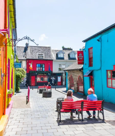 Colourful street view with vibrant buildings, welcoming seating area, and sunlit cobblestones near boutique hotel.