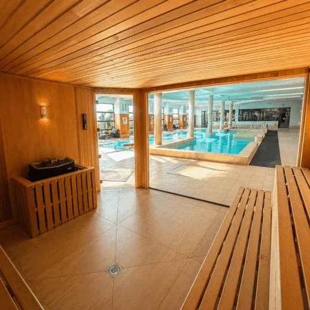 Luxurious indoor pool viewed from a wooden sauna, featuring modern facilities and serene atmosphere.