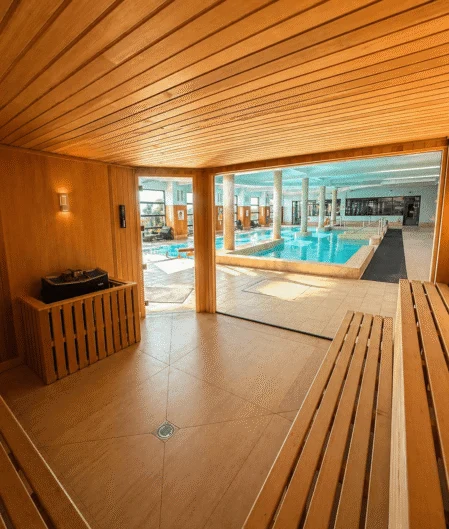 Luxurious indoor pool viewed from a wooden sauna, featuring modern facilities and serene atmosphere.