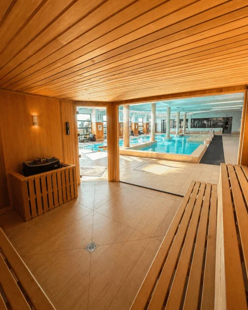 Luxurious indoor pool viewed from a wooden sauna, featuring modern facilities and serene atmosphere.