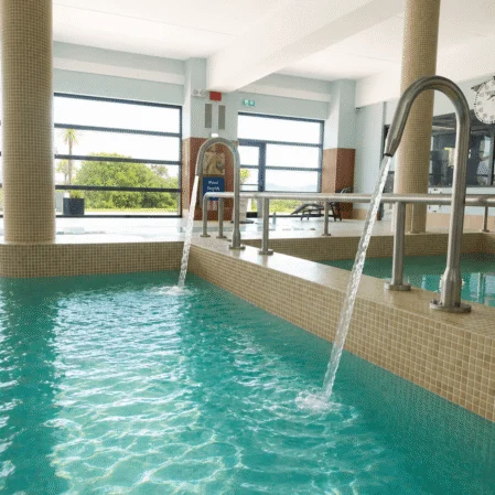 Relaxing indoor pool with soothing water features in modern hotel, surrounded by natural light and serene views.